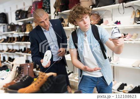 Portrait of positive teenager buying sneakers during shopping in shoe store 112108623