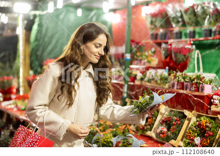 Smiling woman choosing festive home decorations on street Christmas fair Smiling woman choosing festive home decorations on street Christmas fair 112108640