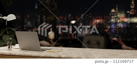 A modern office at night with a city view, featuring a laptop and accessories on a desk. 112109717