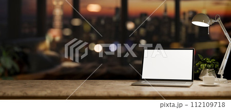 An office desk with a white-screen laptop computer in a modern dark office at night. 112109718