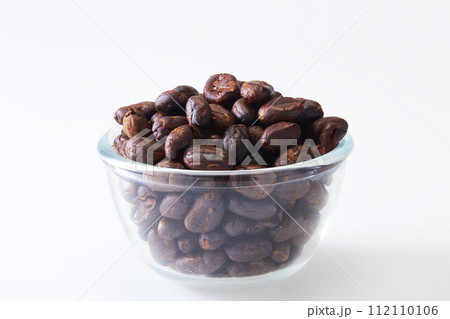 Roasted cocoa beans in a glass bowl on white 112110106