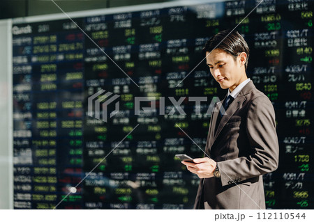 株価の一覧が表示された株価ボードの前でNISAで資産形成を試みる30代の日本人の若い男性 112110544