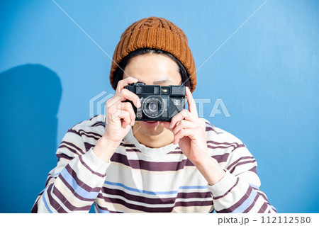 ブルーバックでニット帽をかぶりカメラを構える若い男性 112112580