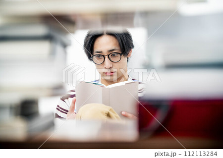 大量の本に囲まれながら本を読む若い男性 112113284