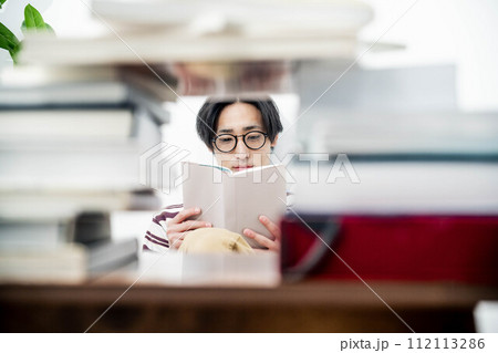 大量の本に囲まれながら本を読む若い男性 112113286