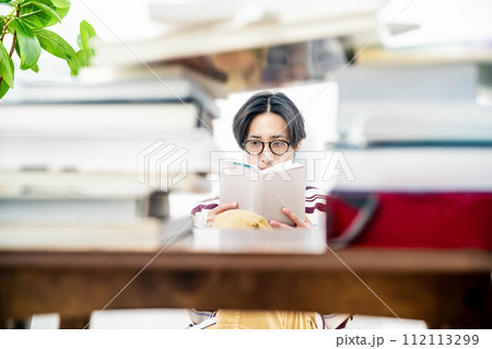 大量の本に囲まれながら本を読む若い男性 大量の本に囲まれながら本を読む若い男性 112113299