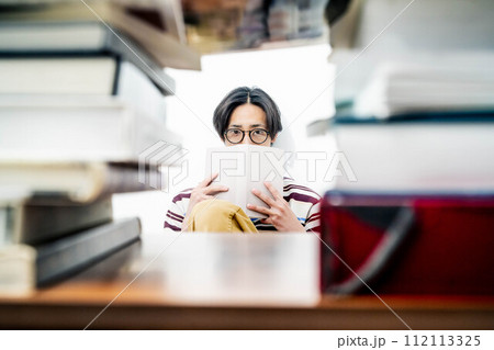 大量の本に囲まれながら本を読む若い男性 大量の本に囲まれながら本を読む若い男性 112113325