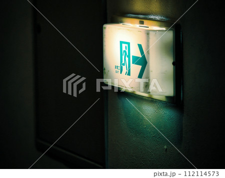 暗がりに汚れた非常口の誘導灯 112114573