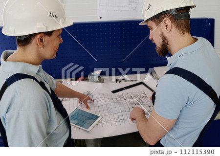 High angle view shot of male and female engineers wearing hardhats working with technical drawings 112115390