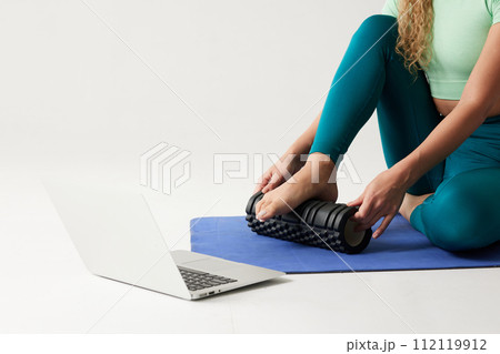girl holding a massage roller while sitting on the floor and near a laptop, massage roller for fitness and yoga, home online workouts girl holding a massage roller while sitting on the floor and near a laptop, massage roller for fitness and yoga, home online workouts 112119912