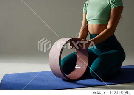young flexible girl doing gymnastics, flexibility and stretching using a yoga wheel online on a white background 112119993