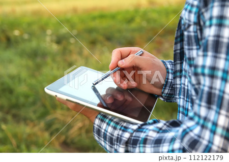 An agronomist farmer uses a digital tablet in a young cornfield at sunrise or sunset. Close-up of hands with tablet screen and stylus An agronomist farmer uses a digital tablet in a young cornfield at sunrise or sunset. Close-up of hands with tablet screen and stylus 112122179