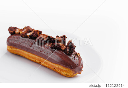 Eclair with Chocolate Cream and Hazelnuts on White Plate 112122914