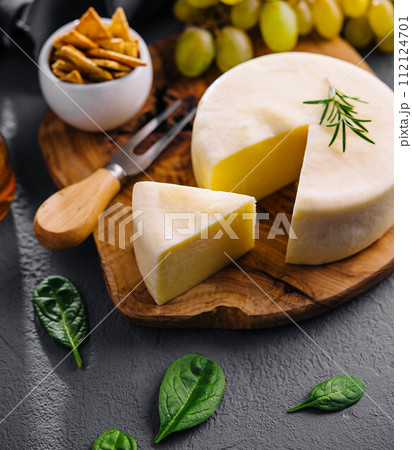 Round cheese on a wooden board and green grapes 112124701