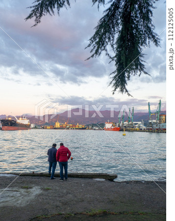 Port area. Container ships in the port. The atmosphere of a cargo seaport. Marine urban landscape. Shipping in Georgia. People on the concrete pier. Port area. Container ships in the port. The atmosphere of a cargo seaport. Marine urban landscape. Shipping in Georgia. People on the concrete pier. 112125005
