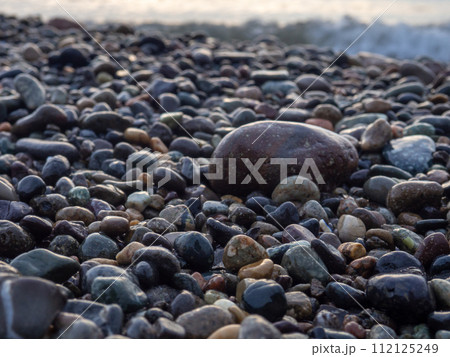 Pebbles on the seashore close-up. Rocky beach. Stones close-up with bokeh. Gray natural background. The concept of rest on the seashore. The Velvet season.   Waves and wet pebbles 112125249