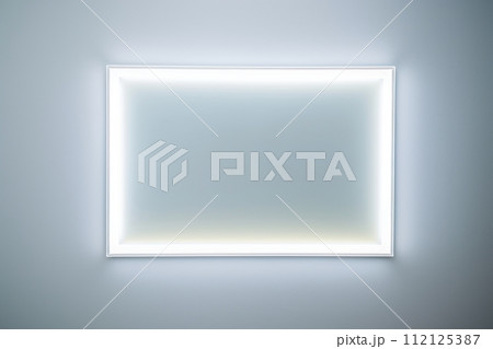 A glowing white rectangle frame on a wall in a minimalist white room 112125387