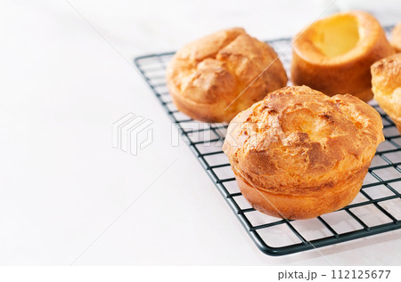 Popovers on a black pastry rack on a white background, copy space. Eggs and butter flavor, tasty snack, easy cooking breakfast. Yorkshire pudding Popovers on a black pastry rack on a white background, copy space. Eggs and butter flavor, tasty snack, easy cooking breakfast. Yorkshire pudding 112125677