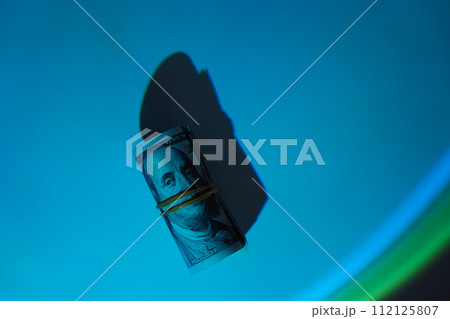 One hundred dollar bills rolled up under hard blue light 112125807