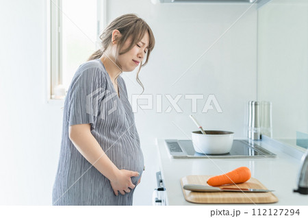 キッチンで料理中にお腹が痛くなる妊婦の女性（陣痛・破水・切迫早産） 112127294
