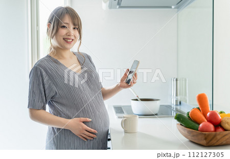 キッチンでスマートフォンを使う妊婦の女性(マタニティ・アプリ・栄養管理・食事管理・食事記録) キッチンでスマートフォンを使う妊婦の女性(マタニティ・アプリ・栄養管理・食事管理・食事記録) 112127305