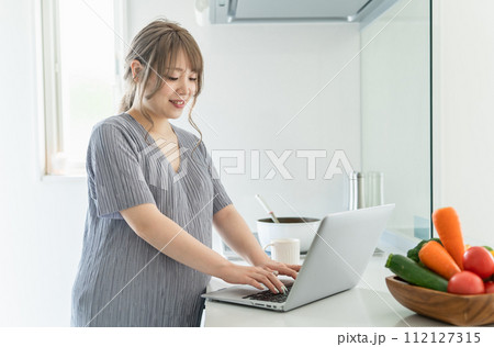キッチンでパソコンで食事日記・食事記録・食事管理をする妊婦の女性 112127315