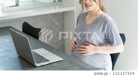 自宅のダイニングでノートパソコンでビデオ通話・テレビ電話をしながらお腹をさする妊婦 自宅のダイニングでノートパソコンでビデオ通話・テレビ電話をしながらお腹をさする妊婦 112127324