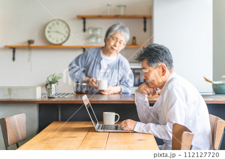 ダイニングでコーヒーを入れてもらいパソコンを見ているシニア男性 112127720