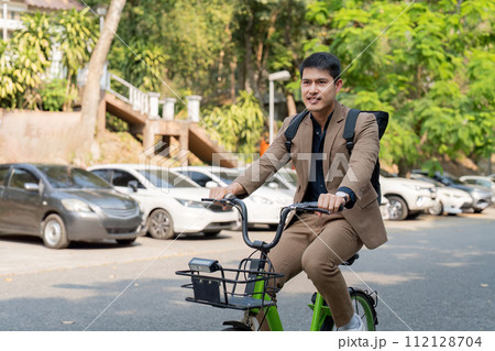 The businessman eco friendly transportation, cycling through the city avenues to go to work. sustainable lifestyle concept The businessman eco friendly transportation, cycling through the city avenues to go to work. sustainable lifestyle concept 112128704