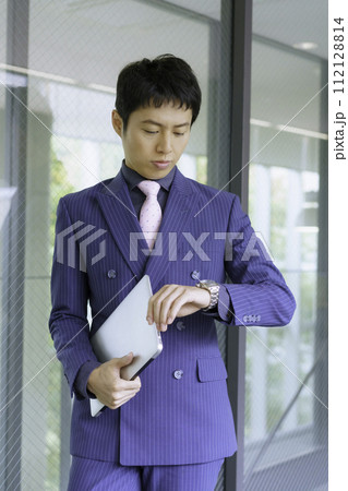 ダブルのスーツを着て時間を気にする若い男性　縦位置　撮影協力:有明教育芸術短期大学 112128814