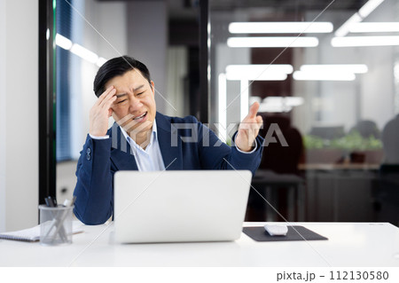 Frustrated chinese boss of company touching forehead with hand while squinting in pain at workplace. Stressed formal male asking employee for bringing medicine for migraine attack relieving. Frustrated chinese boss of company touching forehead with hand while squinting in pain at workplace. Stressed formal male asking employee for bringing medicine for migraine attack relieving. 112130580