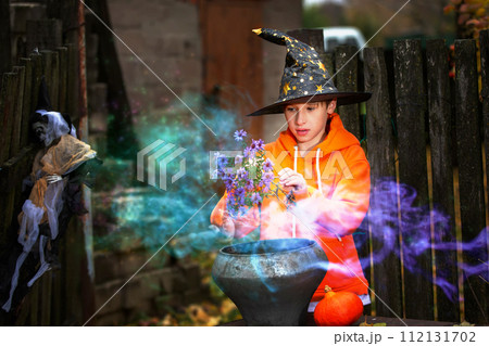 Halloween a child with a magic bowler hat in a sorcerer's hat performs witchcraft against the background of an old creepy house.The wizard boy at the halloween party. Halloween a child with a magic bowler hat in a sorcerer's hat performs witchcraft against the background of an old creepy house.The wizard boy at the halloween party. 112131702