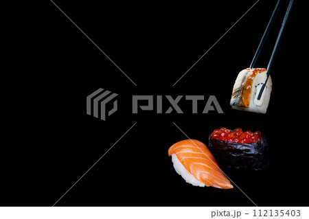sushi on a black background, sushi nigiri, caviar and sushi with eel taken with chopsticks 112135403