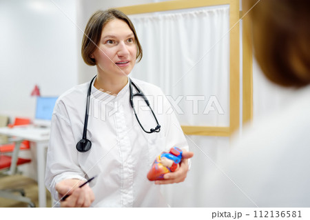 A cardiologist during appointment of patient. Doctor shows anatomical model of human heart and explains about deviations in the structure. Cardiology consultation and treatment A cardiologist during appointment of patient. Doctor shows anatomical model of human heart and explains about deviations in the structure. Cardiology consultation and treatment 112136581