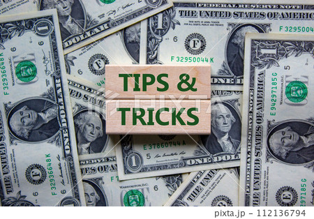 Tips and tricks symbol. Wooden blocks with words 'Tips and tricks'. Beautiful background from dollar bills. Business, tips and tricks concept. Copy space. Tips and tricks symbol. Wooden blocks with words 'Tips and tricks'. Beautiful background from dollar bills. Business, tips and tricks concept. Copy space. 112136794