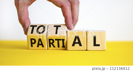 Total or partial symbol. Businessman turns beautiful wooden cubes and changes the word Partial to Total. Beautiful yellow table white background. Business and total or partial concept. Copy space. 112136812