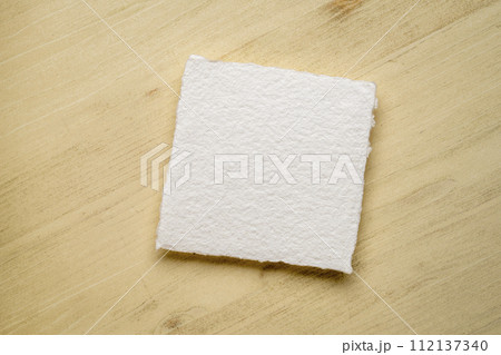 small, square, blank sheet of watercolor paper against wooden background 112137340