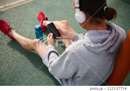 Overhead view of active sportsman wearing headphones, checking sports app on his smart mobile phone 112137754