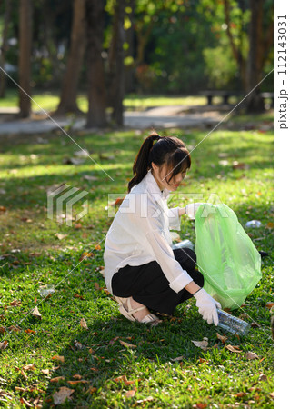 Portrait of young woman picking up litter in the park on a sunny bright day. Environmental protection concept Portrait of young woman picking up litter in the park on a sunny bright day. Environmental protection concept 112143031