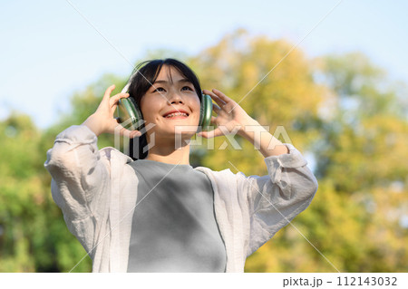 Cheerful happy young woman wearing headphones listening to music in the park on beautiful day Cheerful happy young woman wearing headphones listening to music in the park on beautiful day 112143032