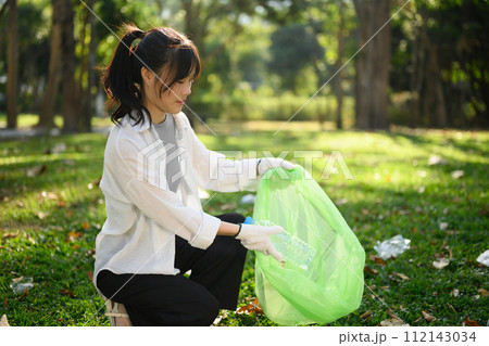 Smiling young woman collecting plastic bottles in the park. Environmental responsibility concept 112143034