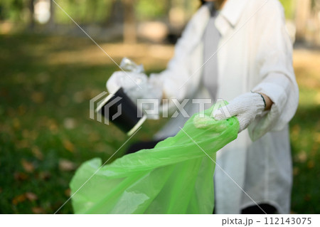 Young woman in gloves collecting garbage in the park. Environmental responsibility concept Young woman in gloves collecting garbage in the park. Environmental responsibility concept 112143075