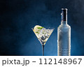 Vodka Cocktail glass and ice-cold bottle on blue degraded background with copy space. 112148967