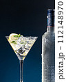 Vodka Cocktail in glass and ice-cold bottle close up on blue degraded background with copy space. Vertical format. 112148970