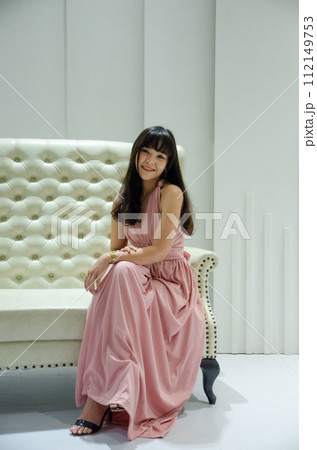 asian young girl is wearing pink dress is sitting on luxury white sofa in studio 112149753