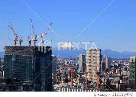 A snow covered Mt Fuji, Fuji-san, as seen from minatoku in central tokyo framed by cranes making high rise buildings 112150476