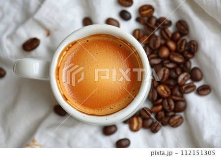 White ceramic cup full of coffee with scattered coffee beans on white fabric 112151305