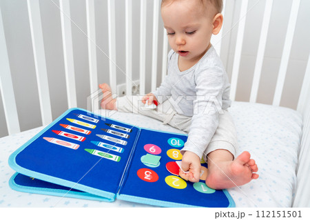 Baby playing with montessori busy book sitting in crib. Concept of smart books and modern toys 112151501
