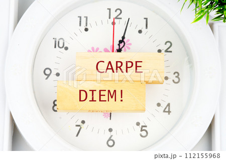 The Latin phrase Carpe Diem, a quote from Horace, means seize the moment. Live in the present written on the wooden blocks on the clock with hands 112155968