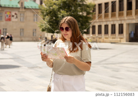 Happy tourist girl with map travels in Europe. Vacation concept by exploring interesting places to travel. Redhead Woman Searching locations at summer sunny day 112156083